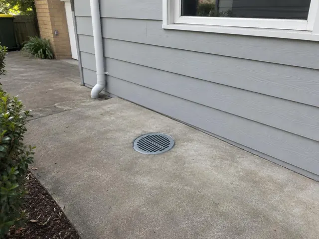Concrete side path with a round drain grate beside a grey house wall in Belrose
